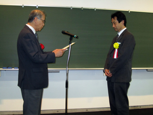 日本ゴム協会長・五十野殿（本学教授）から表彰される河原准教授（写真右側）